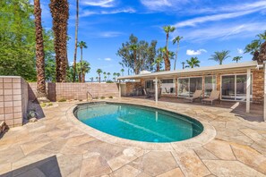 A swimming pool with a stone border, surrounded by palm trees and a covered patio area with outdoor furniture. - El Paseo, 'The Rodeo Drive of Beverly Hills' In Palm Desert. Free Wi FI (Palm Desert)