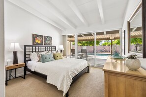 A bedroom with a bed, bedside tables, a desk, and a view of an outdoor pool area. - El Paseo, 'The Rodeo Drive of Beverly Hills' In Palm Desert. Free  Wi FI (Palm Desert)