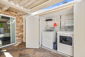A laundry area with two washing machines and a dryer, a stone wall, and a glass door leading to a patio. - El Paseo, 'The Rodeo Drive of Beverly Hills' In Palm Desert. Free Wi FI (Palm Desert)