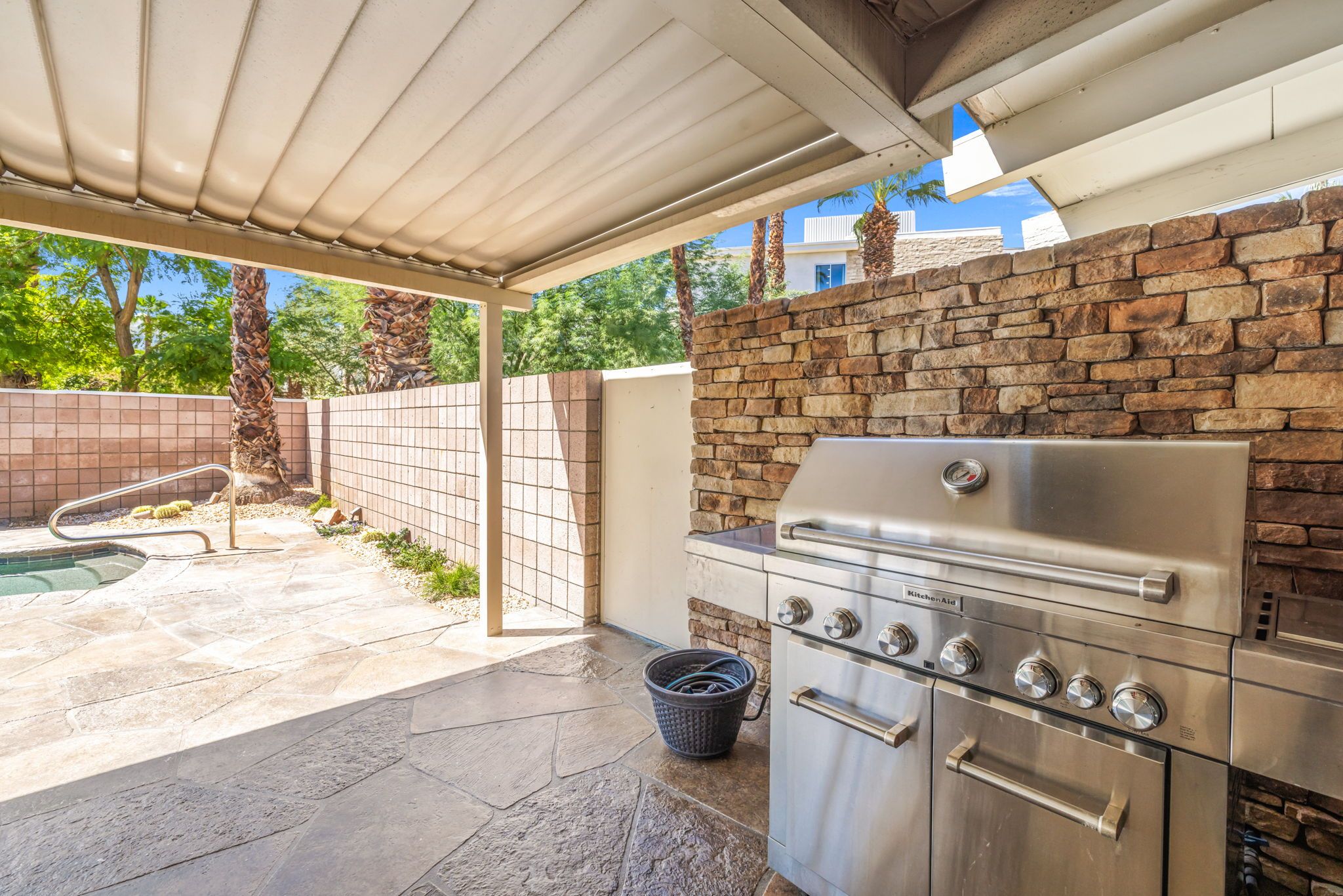 An outdoor kitchen area with a built-in grill, stone wall, and a covered patio.
