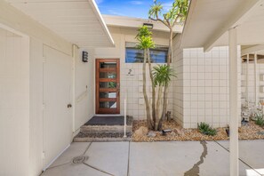 A residential building with a wooden door, a number sign, and a small garden with cacti and a palm tree. - El Paseo, 'The Rodeo Drive of Beverly Hills' In Palm Desert. Free Wi FI (Palm Desert)
