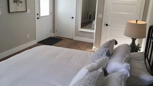 Une chambre avec un grand lit, des murs blancs et une porte donnant sur une salle de bain.