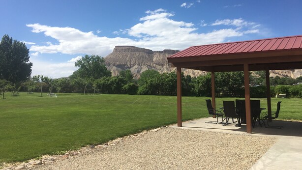 Un espace extérieur aménagé avec des tables et des chaises, protégé par un auvent, une pelouse bien entretenue et une vue sur une chaîne de montagnes sous un ciel dégag é.