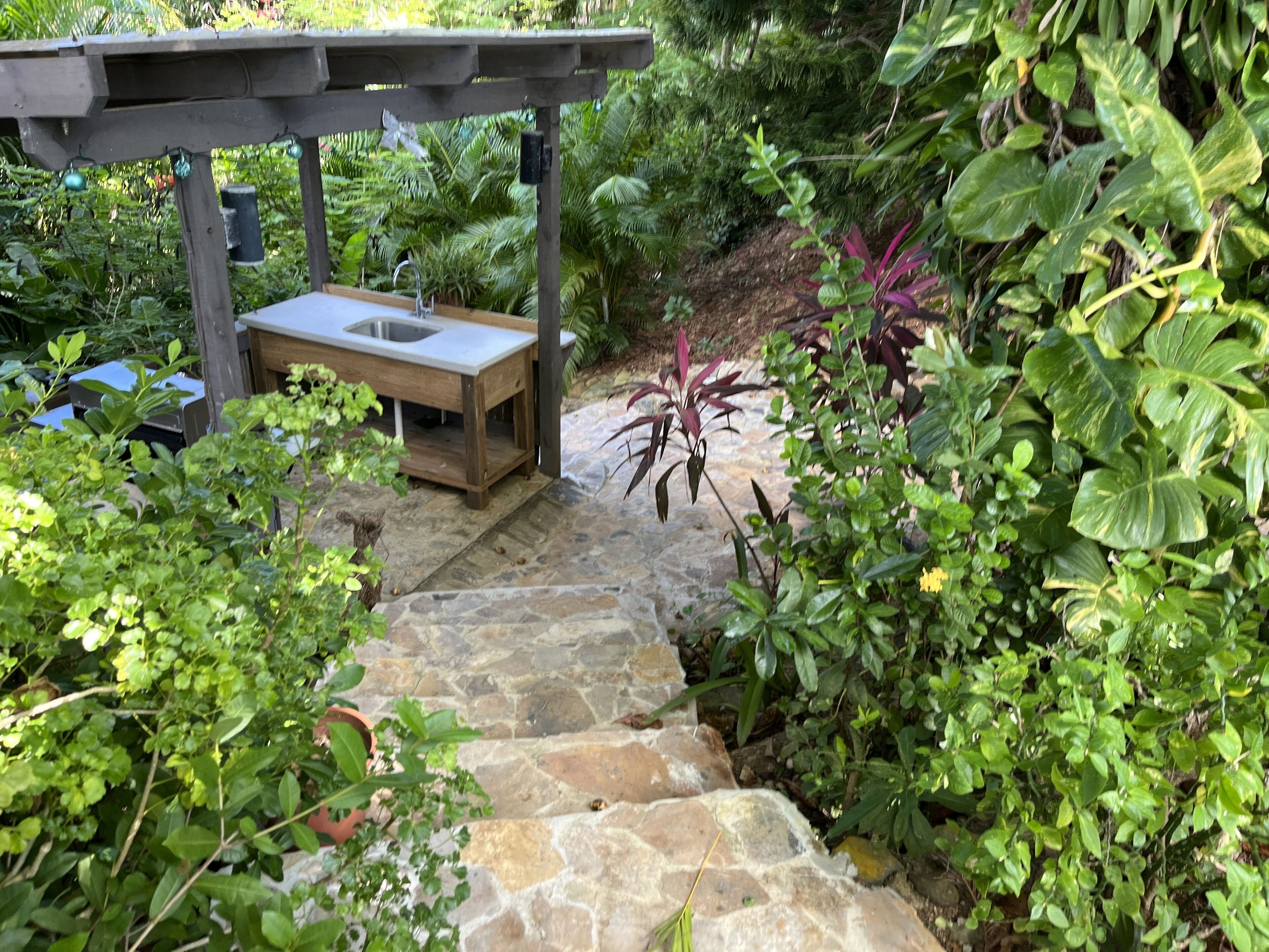 A stone pathway leading to a wooden pergola with a sink.