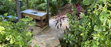 A stone pathway leading to a wooden pergola with a sink.