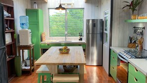 A kitchen with wooden floors, a central island, green cabinets, a stainless steel refrigerator, and a window overlooking greenery.