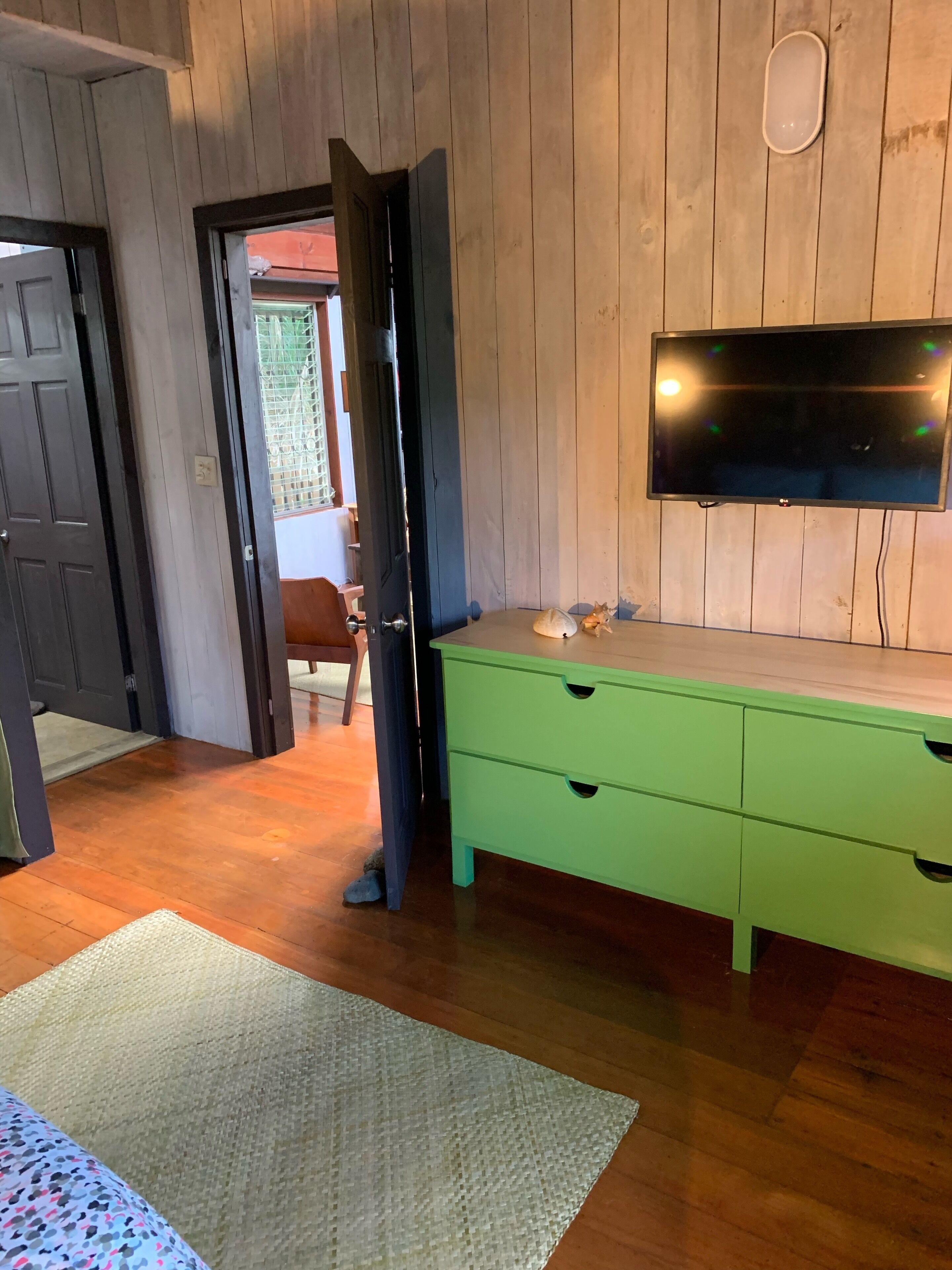 Habitació amb parets de fusta, un taulell verd, televisió penjada a la paret i una porta que dóna a una altra habitació.