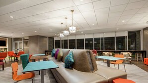 A modern lounge area with seating, tables, and a large window providing a view. - Home2 Suites by Hilton Sarasota - Bradenton Airport, FL (Sarasota)