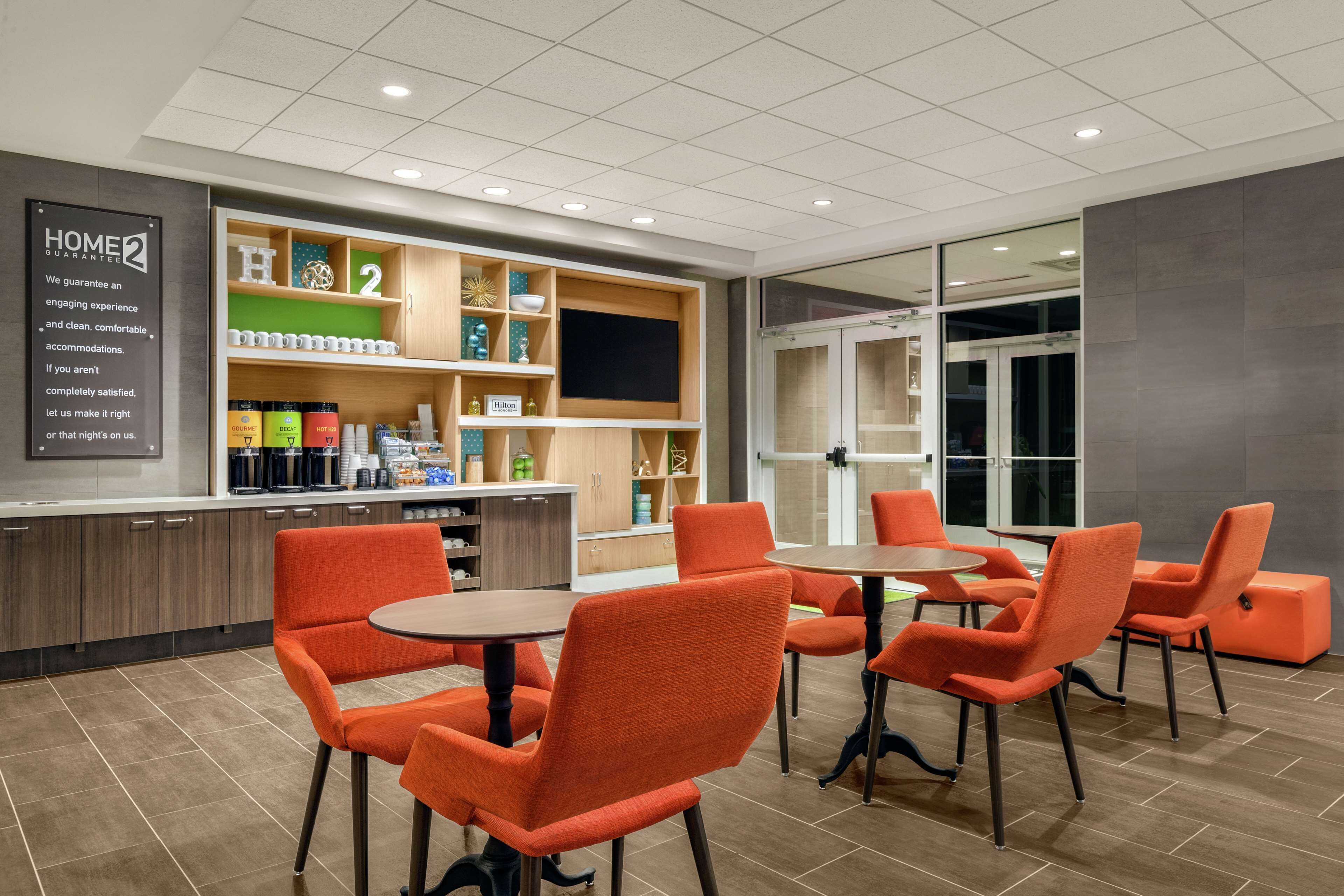 Eine moderne Hotelhalle mit orangefarbenen Sesseln und Tischen, einem Empfangsbereich und einer Übersicht über die angebotenen Annehmlichkeiten.