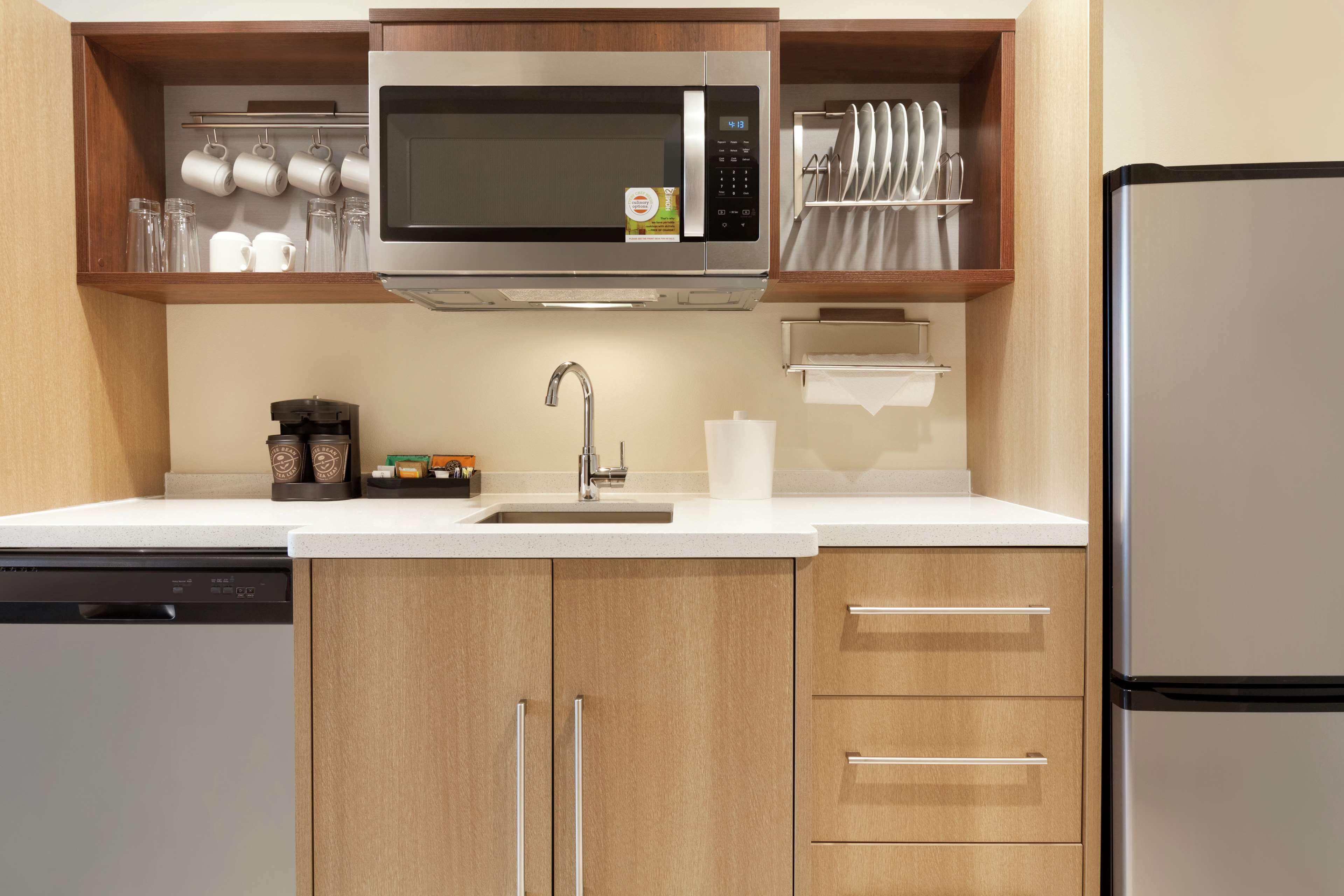 Une cuisine moderne dotée d’un four à micro-ondes encastré, d’appareils électroménagers en acier inoxydable, de meubles de rangement en bois et d’un lave-vaisselle.