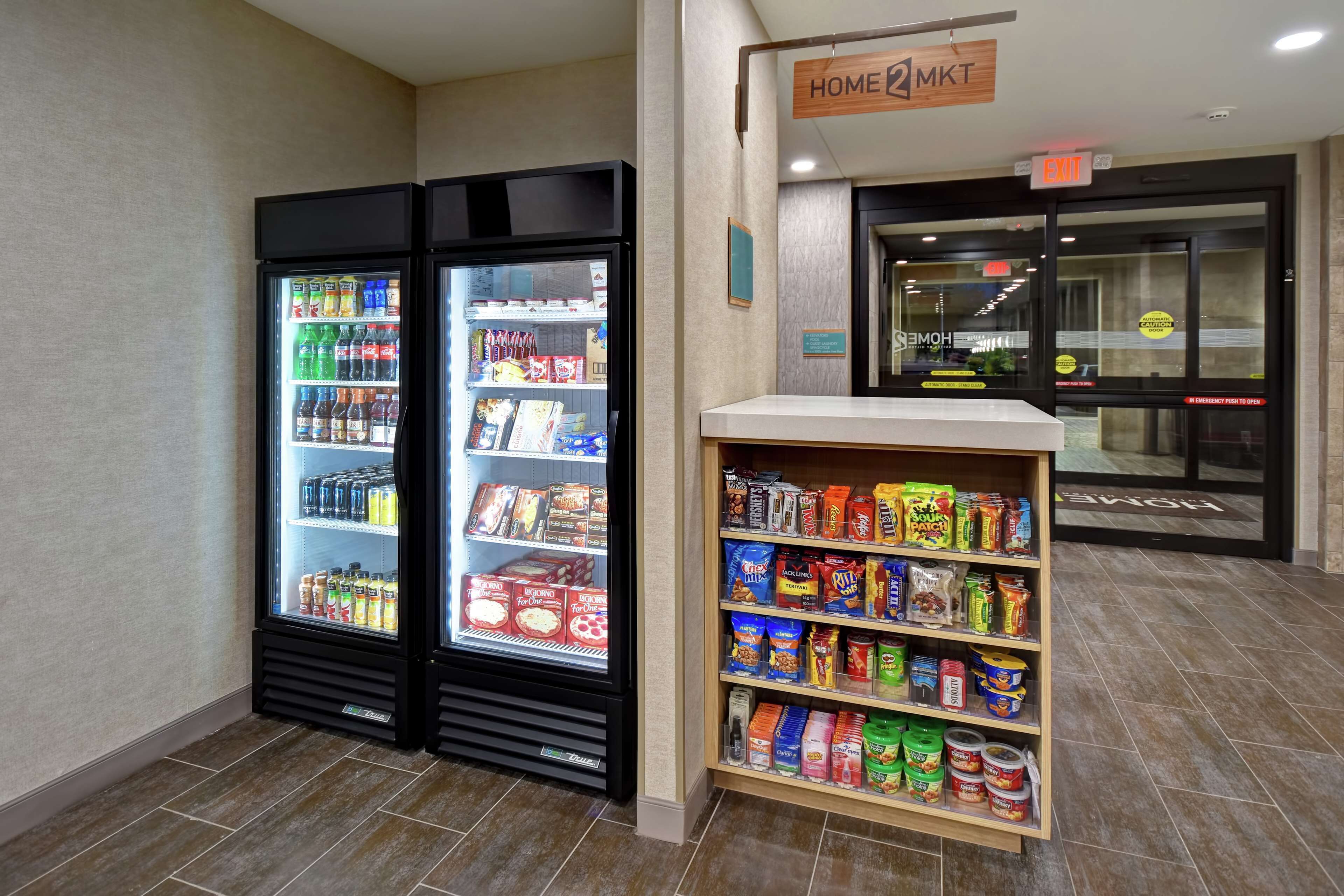 Un área de venta con bebidas refrigeradas y aperitivos, y una estantería llena de diferentes productos alimenticios.