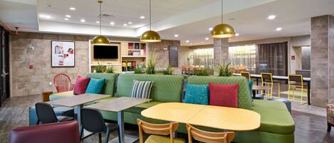 A modern restaurant with a green sofa, yellow table, and red chairs.