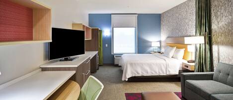 A hotel room with a bed, a desk with a chair, a sofa, a TV, and a window with curtains.