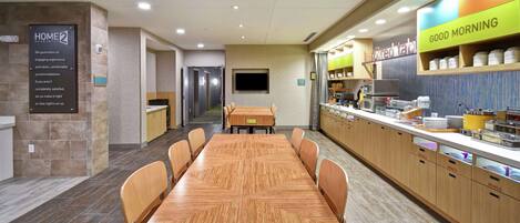 A modern hotel room with a wooden dining table, chairs, a kitchen area, and a breakfast bar.