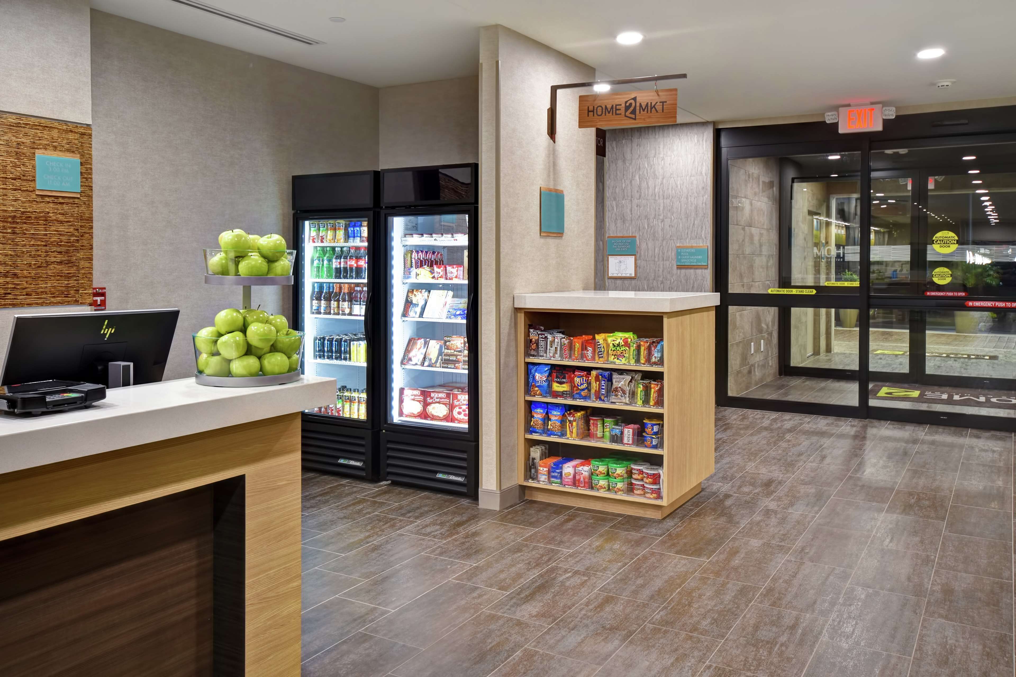 Zona de recepción con mostrador, computadora, refrigerador con bebidas y estante con aperitivos.