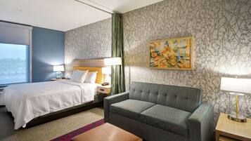 A hotel room with a bed, a sofa, a small table, a lamp, and a painting on the wall.