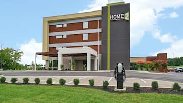 A modern hotel with a prominent 'HOME 2' sign, a covered entrance, and a landscaped front area with small bushes.