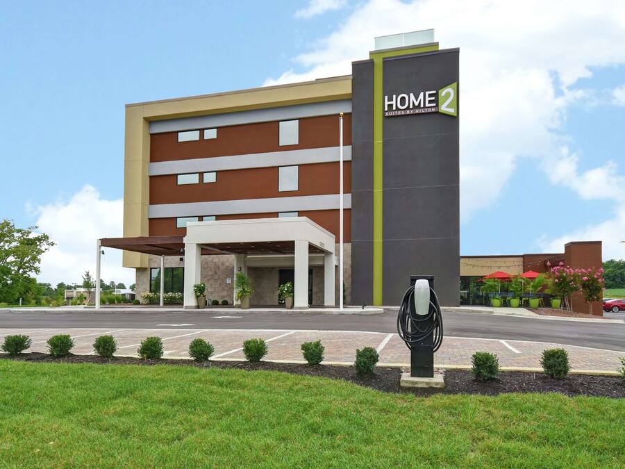 A modern hotel with a prominent 'HOME 2' sign, a covered entrance, and a landscaped front area with small bushes.