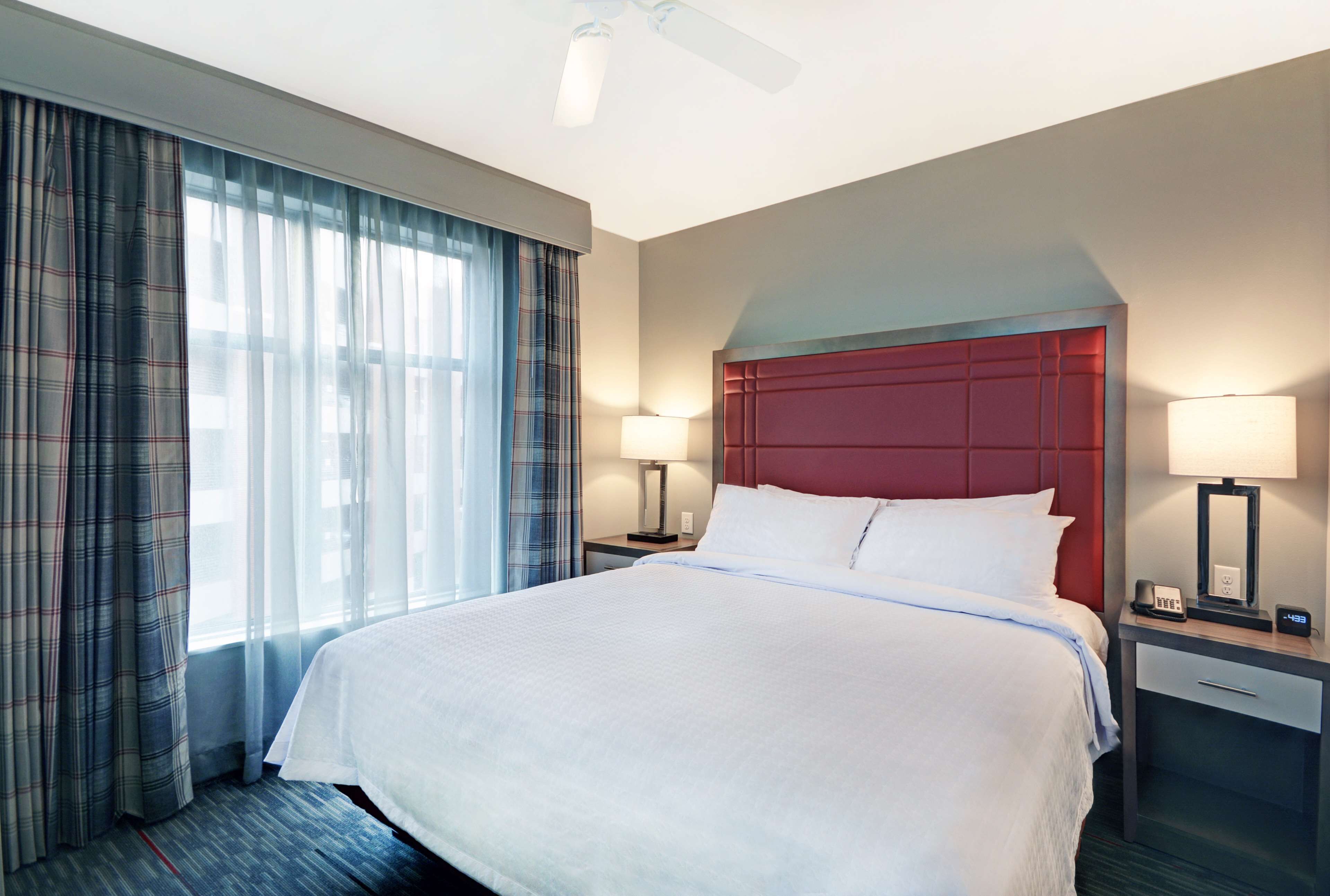 A hotel room with a large bed, two bedside tables with lamps, a red headboard, and a window with curtains.