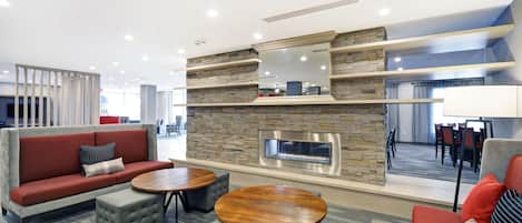 A modern lounge area with a stone fireplace, sofas, and round tables.