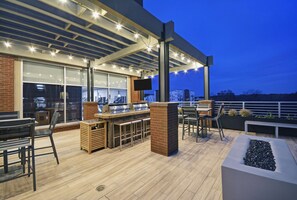 An outdoor patio area with a bar, seating, and a TV screen. - Homewood Suites by Hilton Athens Downtown University Area (Athens)