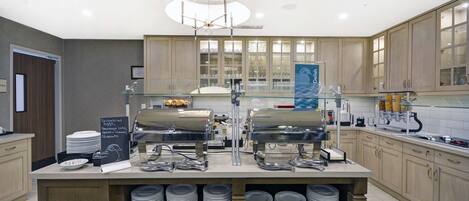 A buffet setup with multiple serving stations, a central island with stacked plates, and a sign indicating food options.