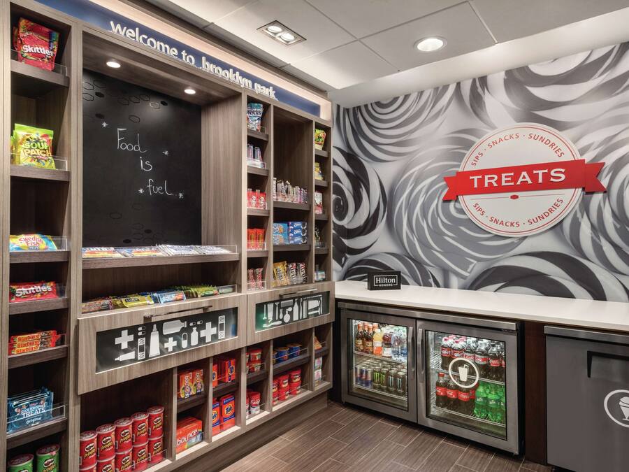 A snack and sundries section with shelves stocked with various snacks, a chalkboard with motivational writing, and a branded sign for treats.