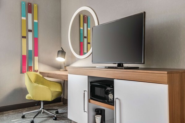 A modern hotel room with a flat-screen TV, a yellow armchair, a coffee maker, and a microwave.
