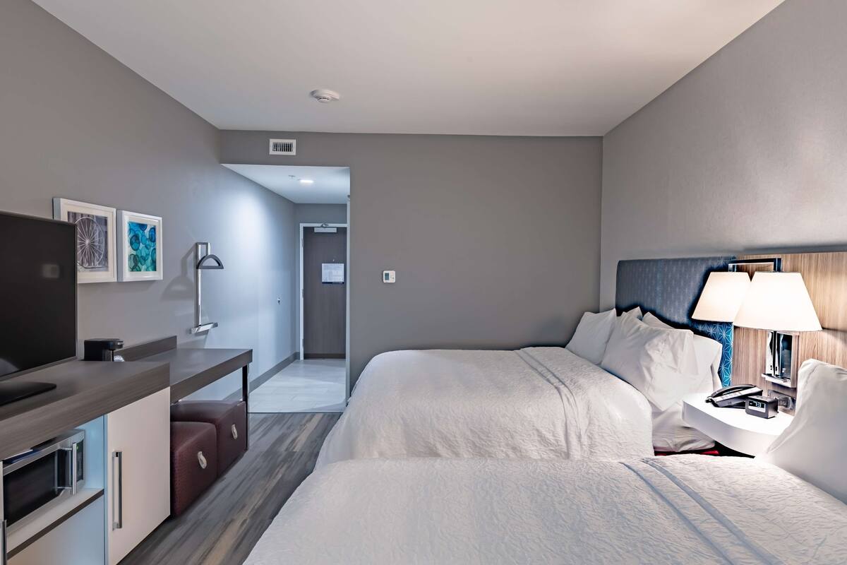 A hotel room with a bed, a desk, a chair, a TV, and a lamp.