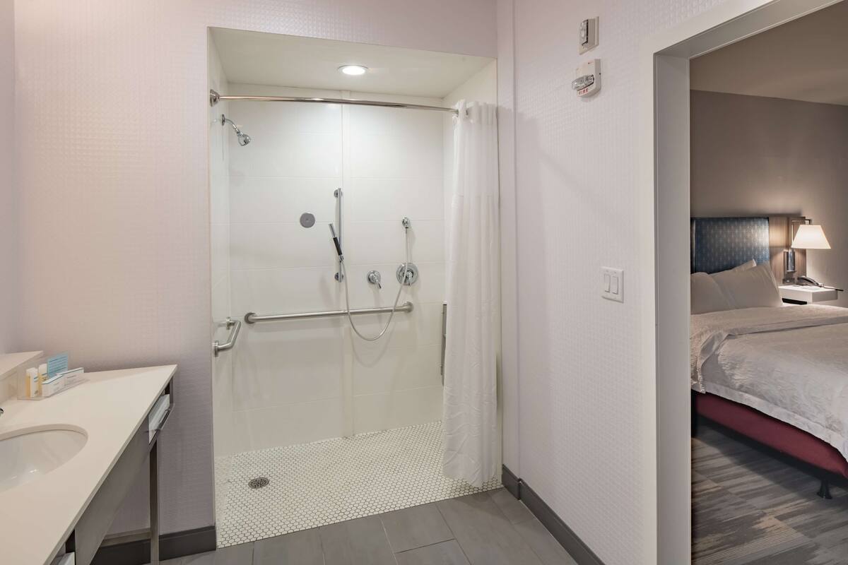 A hotel room with a shower, a bed, a bedside table, and a lamp.