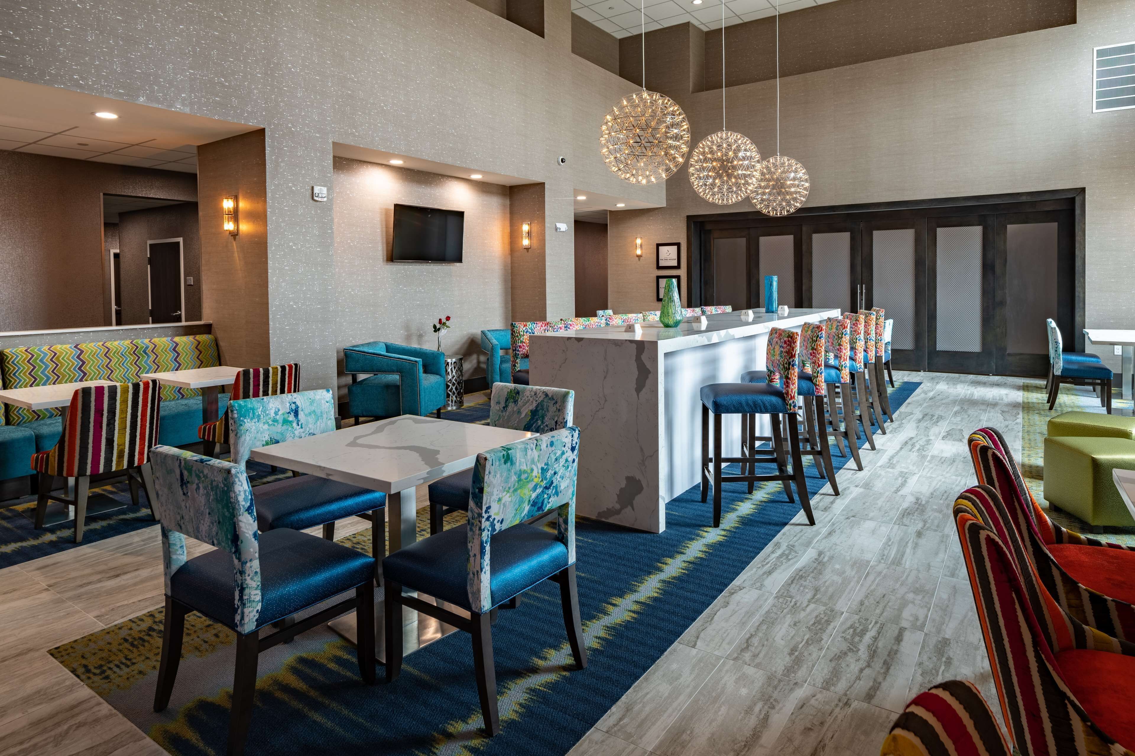 A modern dining area with a central bar, multiple seating options including booths and tables, and a patterned floor.