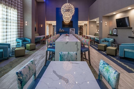 A spacious lobby with a central marble reception desk, blue upholstered seating, and a large chandelier.