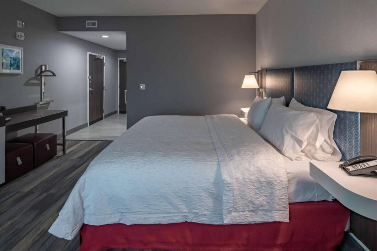 A hotel room with a bed, bedside table, lamp, and a phone.