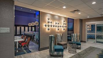 A modern hotel lobby with a breakfast area, seating with patterned upholstery, and a decorative wall with spherical elements.