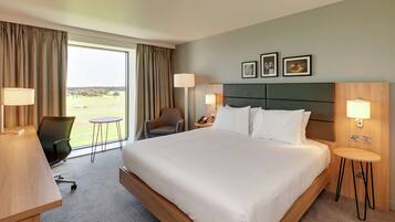 A hotel room with a large bed, two bedside tables, a desk, a chair, and a view of the outdoors.