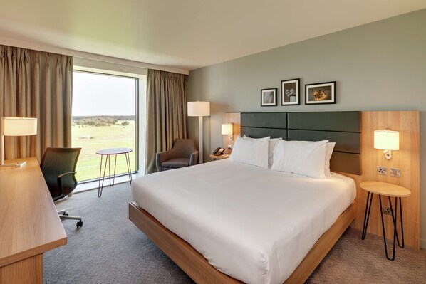A hotel room with a large bed, two bedside tables, a desk, a chair, and a view of the outdoors.