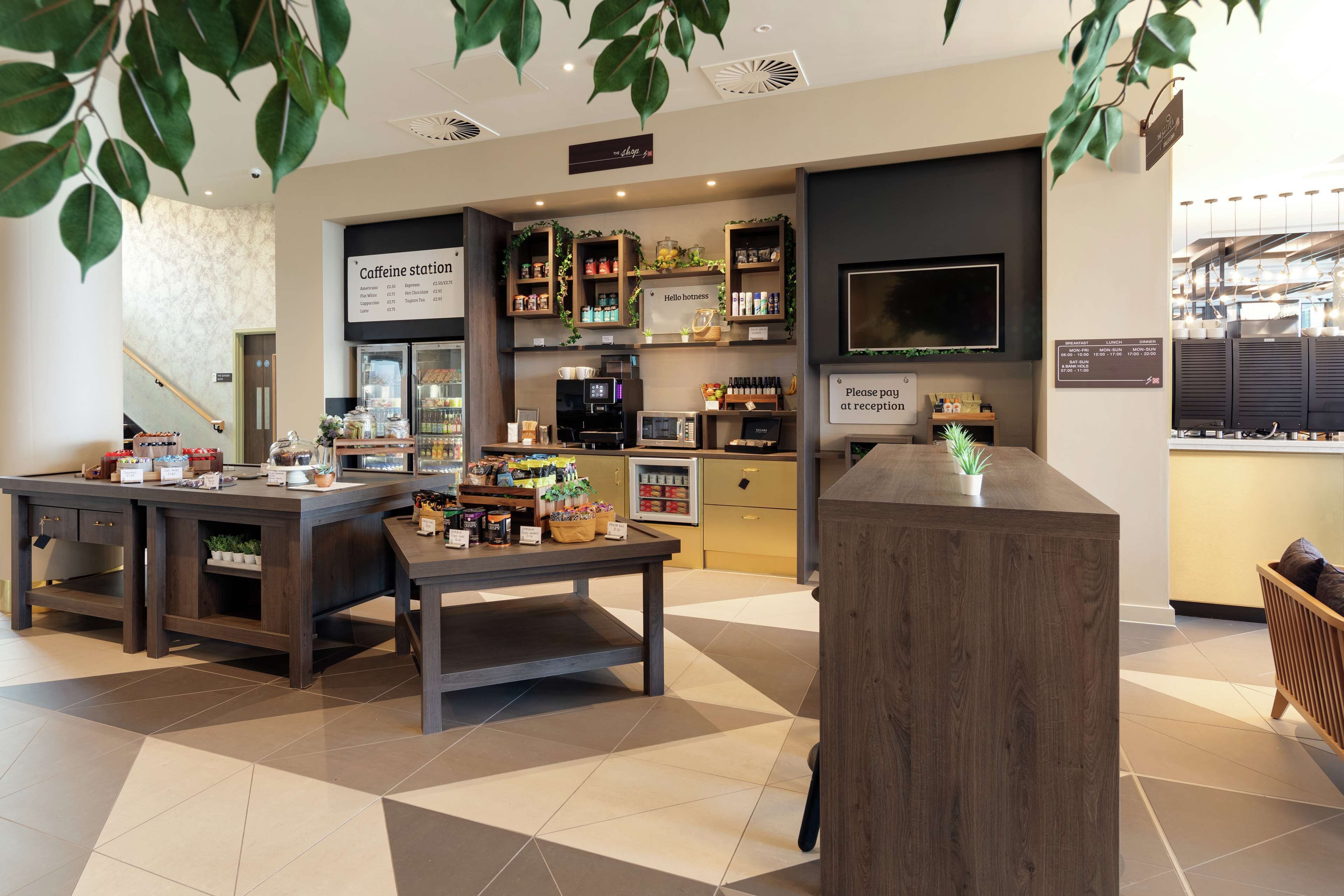 A coffee shop interior with a reception desk, coffee machines, shelves with products, and a sign indicating payment at reception.