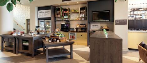 A coffee shop interior with a reception desk, coffee machines, shelves with products, and a sign indicating payment at reception.