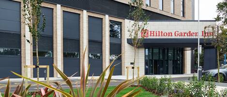 A Hilton Garden Inn with a modern brick facade, large windows, and a landscaped garden area in front.