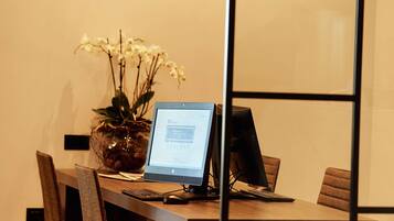 Una sala de conferencias con una mesa de madera, un monitor de computadora y un jarrón con flores blancas.