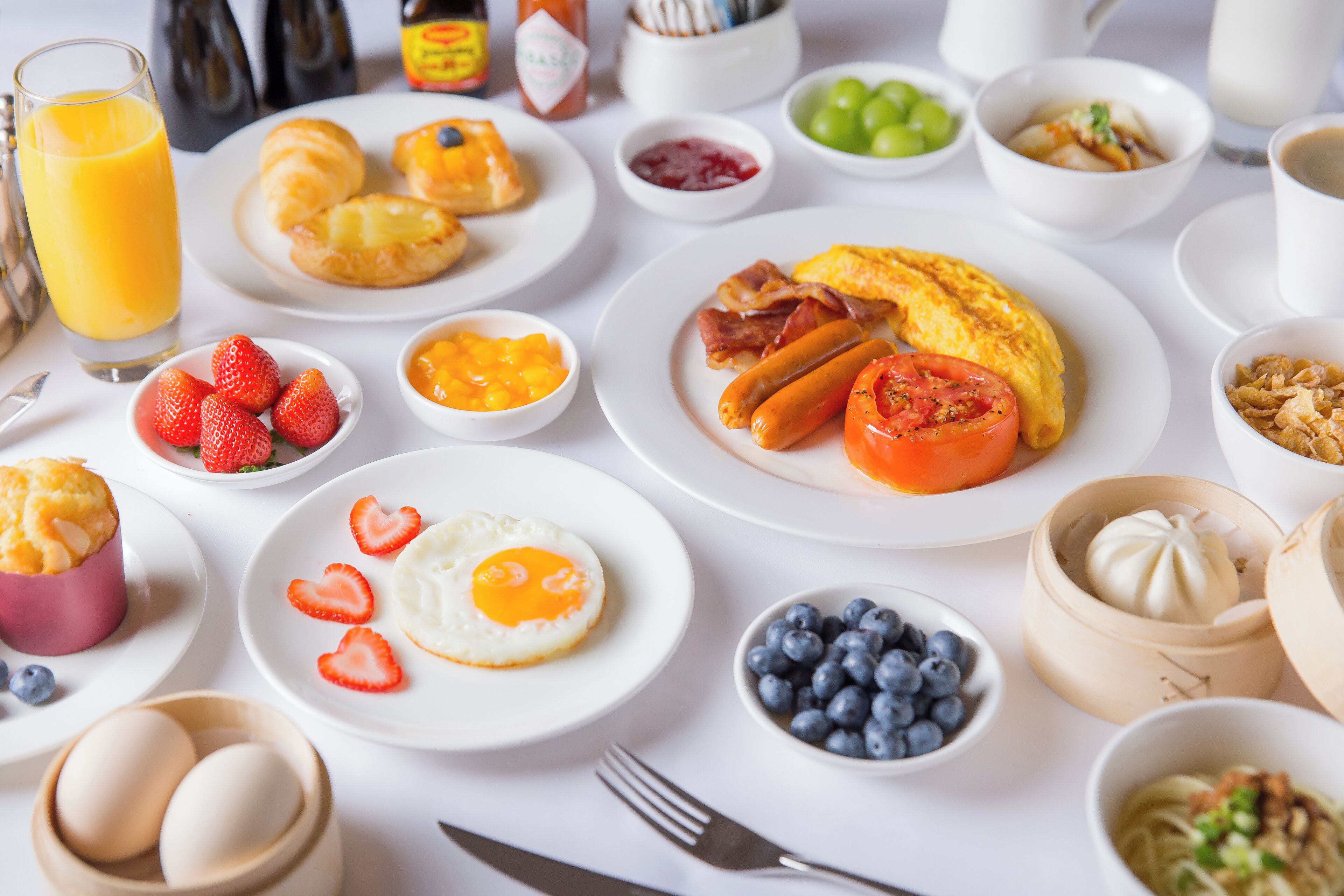A breakfast spread with various dishes including eggs, sausages, tomatoes, and fruits.