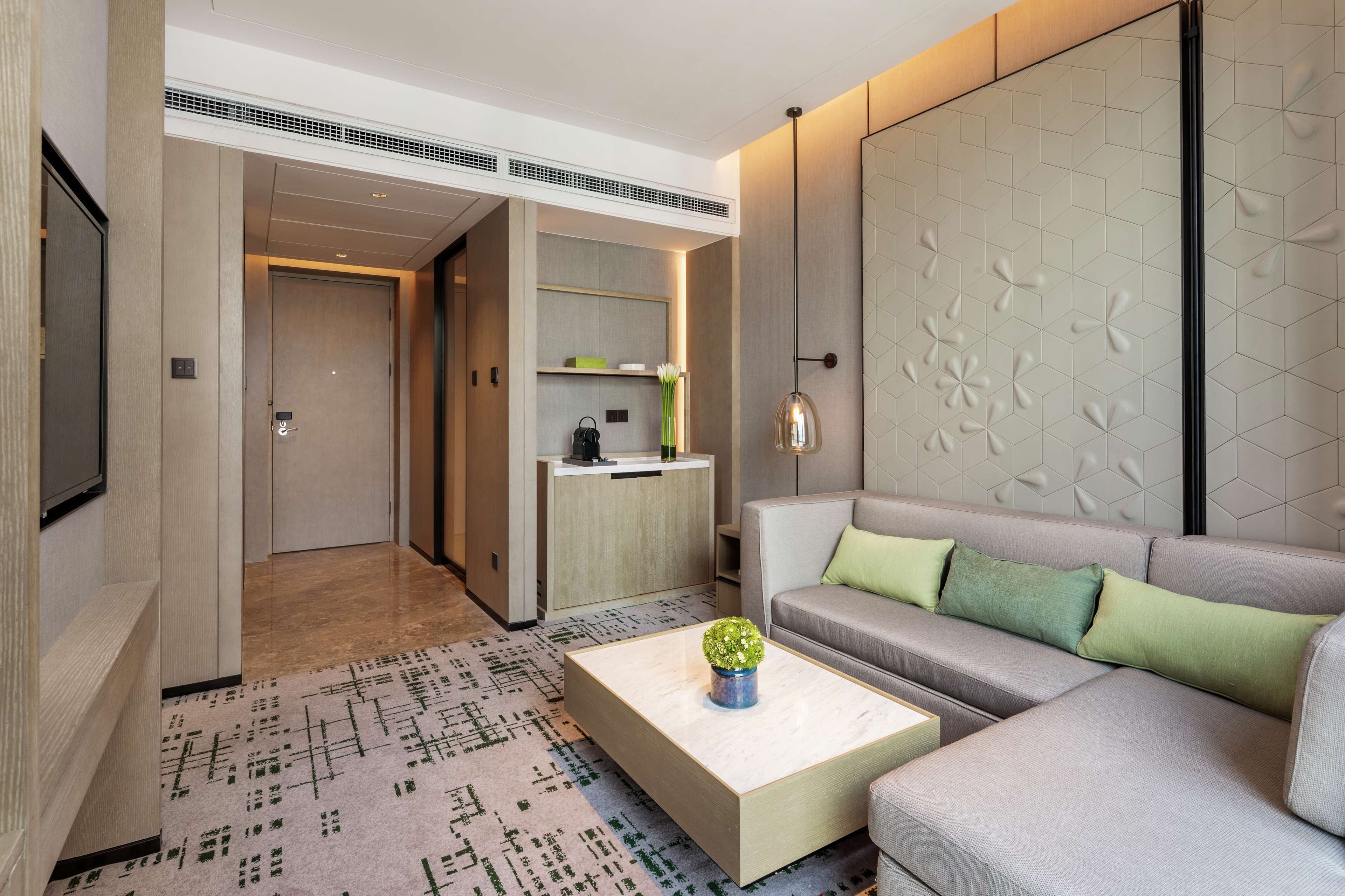 Quarto de hotel moderno com sofá, mesa de centro, cozinha e corredor que dá para outro quarto.