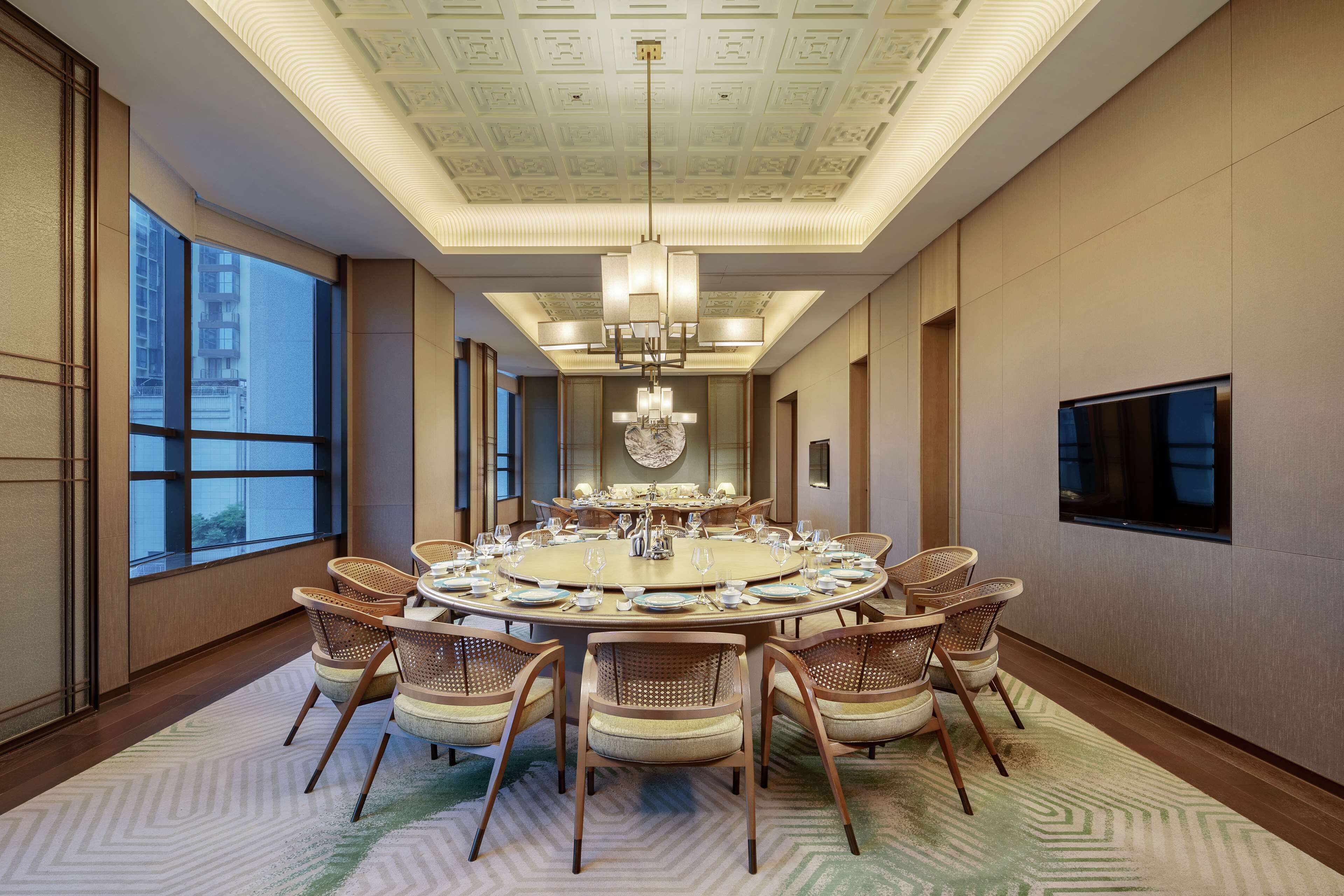 A spacious conference room with a round table, comfortable chairs, and a large chandelier.
