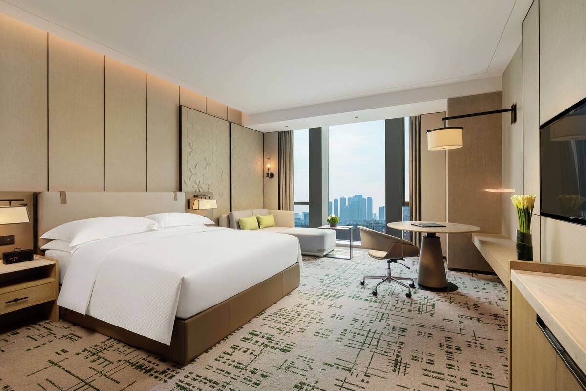 Habitación de hotel moderna con una cama grande, un escritorio, una silla y vistas al horizonte de la ciudad.
