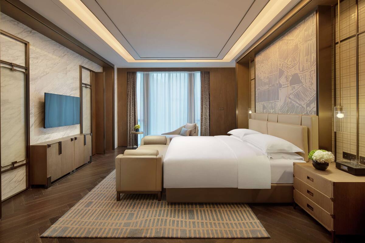 Una habitación de hotel moderna con una cama grande, televisión, escritorio y vistas a un paisaje urbano por la ventana.