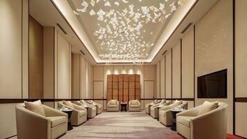 A spacious hotel lobby with multiple seating areas, a large flat-screen TV, and a decorative ceiling feature.