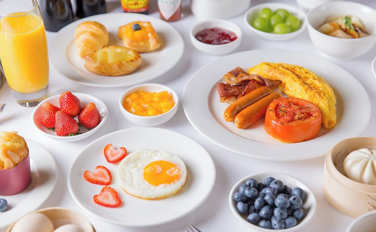 Una mesa de desayuno con diversos platos, incluyendo huevos, salchichas, tomates, fresas y arándanos.