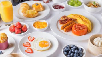 Una mesa de desayuno con diversos platos, incluyendo huevos, salchichas, tomates, fresas y arándanos.