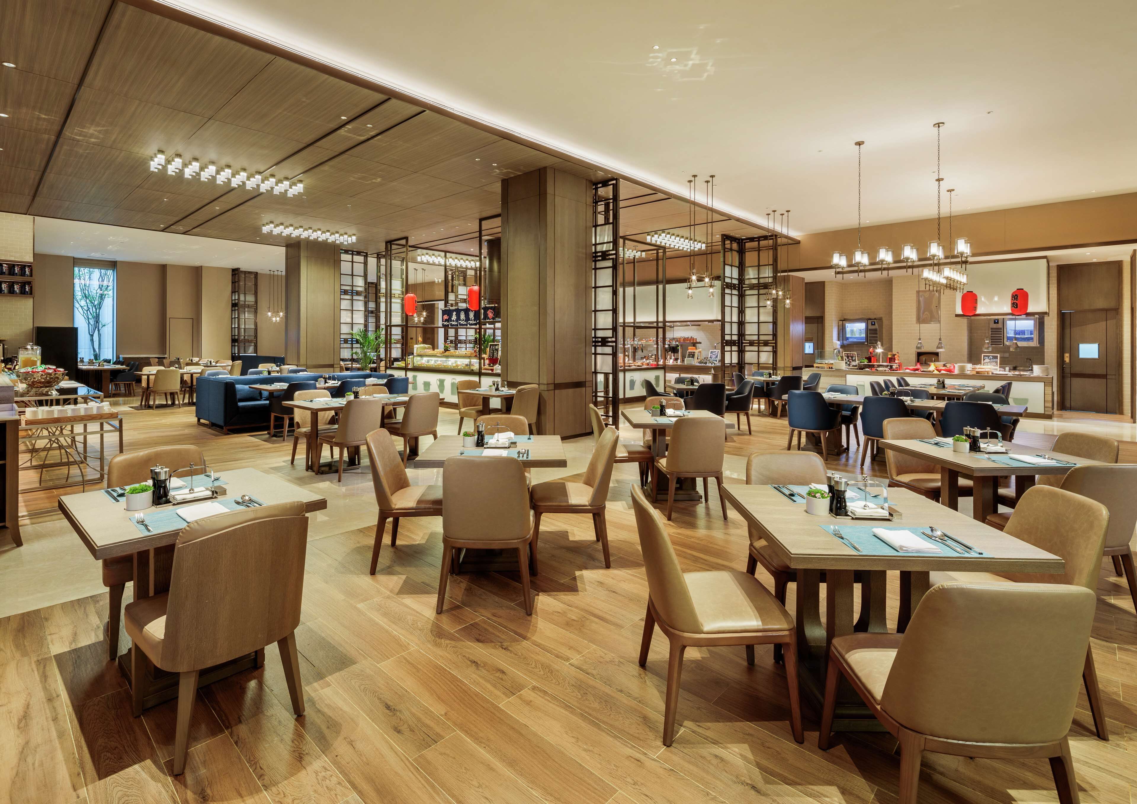 A modern restaurant with wooden flooring, multiple dining areas, and contemporary lighting fixtures.