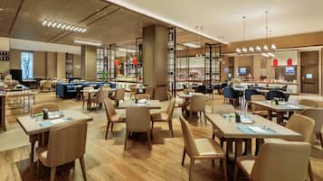 Un restaurante moderno con suelo de madera, varias zonas de comedor e iluminación contemporánea.